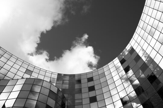Abstract modern architecture shows a curved glass facade under a sky with clouds creating a sleek building form in refined monochrome contrast