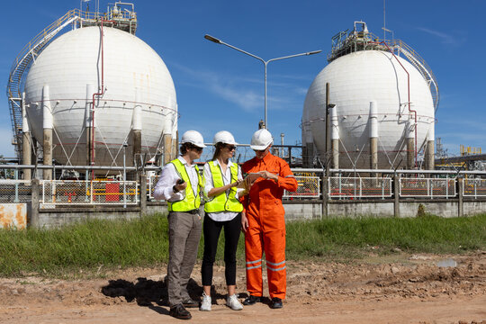 Industrial Engineer Using Digital Tablet for Predictive Maintenance in Oil and Gas Refinery. Team of Engineers Discussing Safety Protocols at Large Scale Oil Refinery Facility.