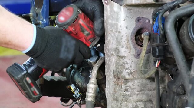 Mechanic screws car exhaust system part with electric screwdriver in repair shop closeup. Worker hands fix vehicle gases collector at station