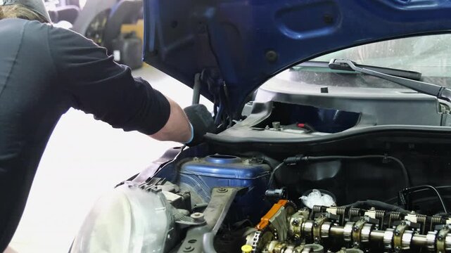 Man mechanic in uniform pushes car with open hood at service station backside view. Worker prepares auto for repair in shop slow motion