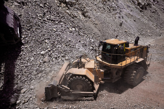 Raw power meets precision,a wheel dozer pushes through the demanding terrain of a high-altitude open pit mine under a heavy overcast sky, with a Caterpillar haul truck standing by in the background. 