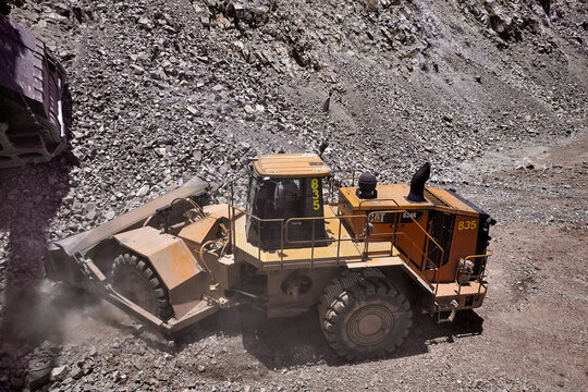 Raw power meets precision,a wheel dozer pushes through the demanding terrain of a high-altitude open pit mine under a heavy overcast sky, with a Caterpillar haul truck standing by in the background. 