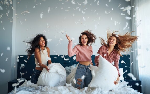 Three happy friends having a playful pillow fight in a stylish bedroom with feathers flying