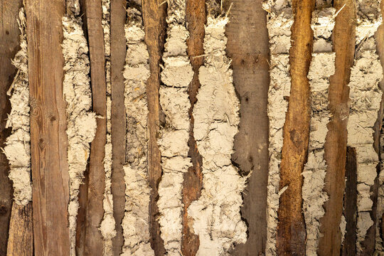 Close-up of old adobe wall with wooden laths, clay plaster, straw fibers and cracks, showing traditional rural building material texture.