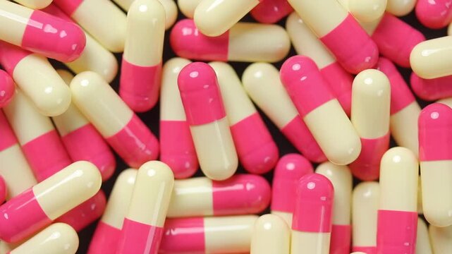 Pile of pink and yellow hard gelatin capsules rotating slowly. Top view shot