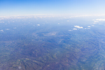 Fototapeta premium High-altitude aerial view of rugged hills, valleys, vegetation, and scattered clouds under blue sky
