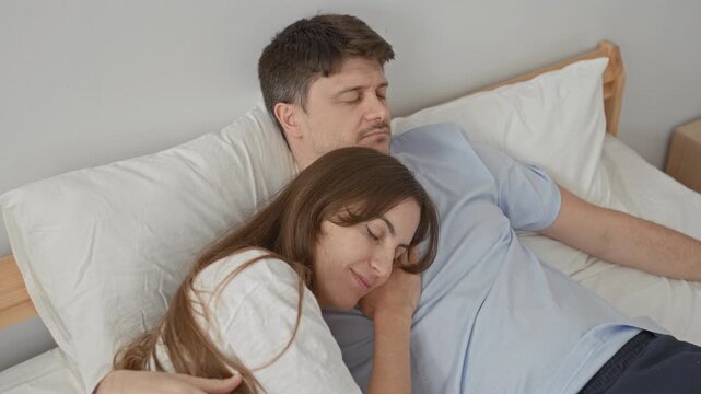 Man and woman cuddled on a bed, woman resting head on man's chest with arm around him in a bedroom building; love trust serenity.