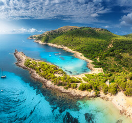 Fototapeta premium Aerial view of Cala Agulla beach, turquoise water, white sand, lush greenery, yachts and boats anchored in the picturesque bay of Mallorca, Balearic Islands, Spain, Summer travel. Top drone view