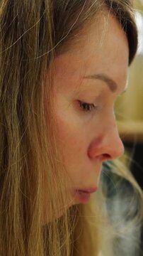 Woman eats green ceasar salad while talking with friend during lunch break. Chew action shows lettuce on fork while face expresses relaxed mood in cafe