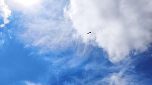 Lone paraglider flying freely against a beautiful blue sky with scattered white clouds. The sun shines brightly, creating a serene and epic scene in Demanovska Dolina, Slovakia