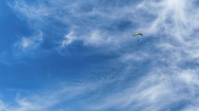 Paraglider flying gracefully across a vivid blue sky filled with delicate, wispy white clouds. This scenic view captures the freedom and serenity of extreme sports in Demanovska Dolina, Slovakia