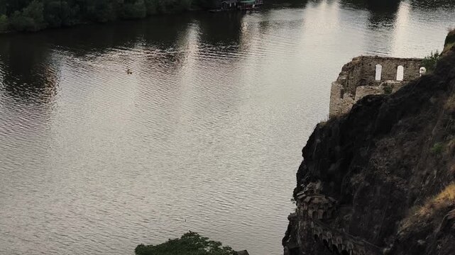 High angle view of a lone person kayaking on the vltava river in prague, passing the historic rocky cliff below vysehrad castle