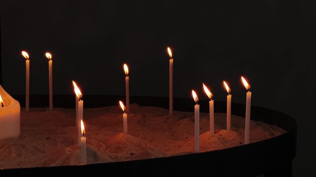 Many thin white votive candles flickering inside a dark church. The flames glow, creating a spiritual and peaceful atmosphere for prayer