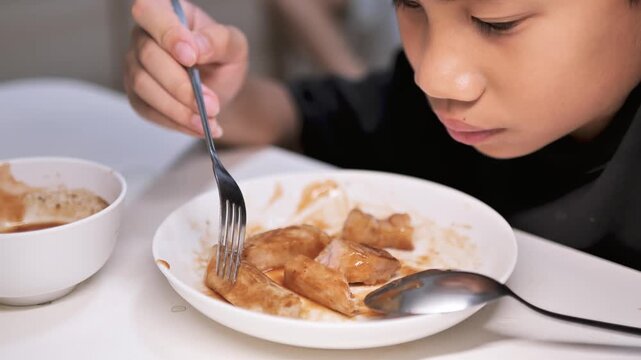 Close-up of a child poking food with a fork without eating, showing a negative reaction and disinterest in the meal. The image reflects picky eating behavior, food refusal, and challenges in children&rsquo;