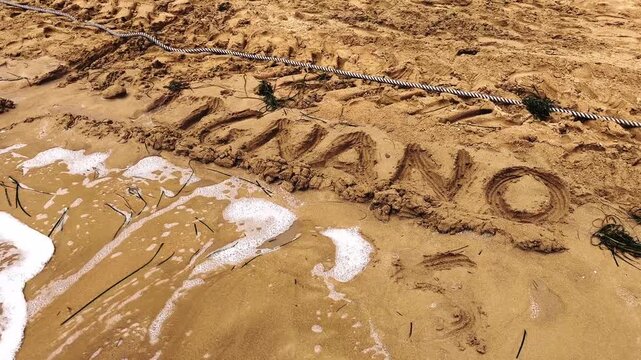Gentle sea foam washing over the sandy shore, gradually erasing the word lignano written on the beach. A concept of memories and passing time in Pineta, Lignano Sabbiadoro, Italy