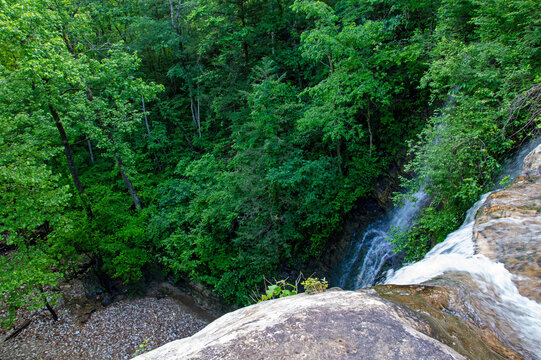 From the top looking down at waters flowing to the bottom surrounded by green trees. Bokeh.
