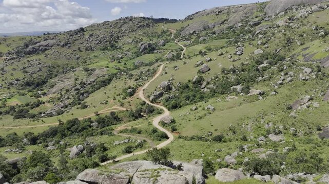 Drone flies past boulders on hill overlooking hiking trail on a sunny day at Sibebe Rock near Mbabane, Eswatini