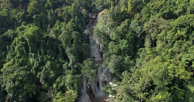 Aerial zoom out reveal of the turquoise Kuang Si Falls cascading through tropical jungle, Luang Prabang, Laos