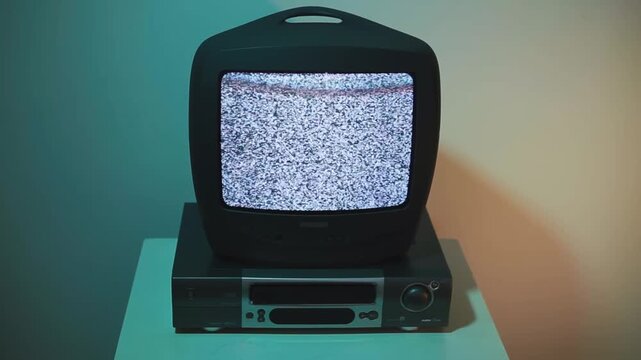 Close-up of an old 1990s CRT television sitting on a wooden nightstand in a dimly lit room. Screen shows classic black and white static noise, nostalgic vintage analog TV from the 90s and early 2000s.