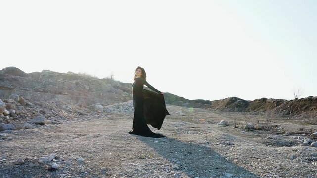 Elegant woman in black flowing dress posing in quarry at sunset