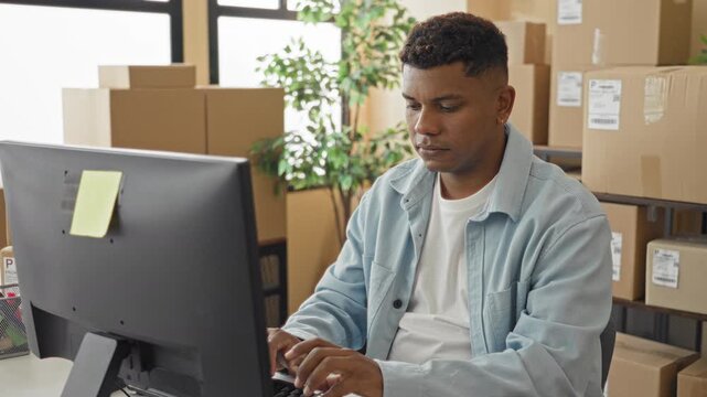 Man at computer surrounded by stacked boxes making a heart with hands near keyboard in a building; gratitude customer care.