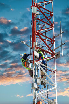 few technicians climbing a telecommunications tower at sunset for maintenance to perform repairs.