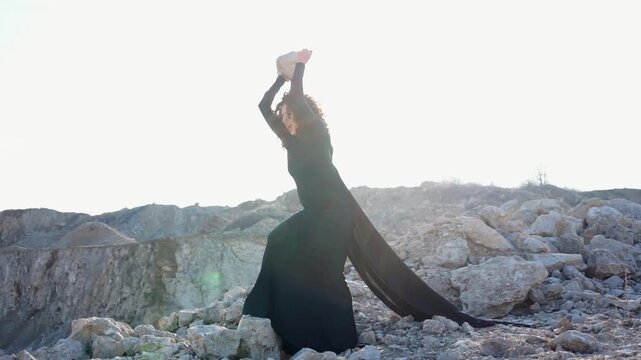 Woman in flowing black dress throwing stone in quarry