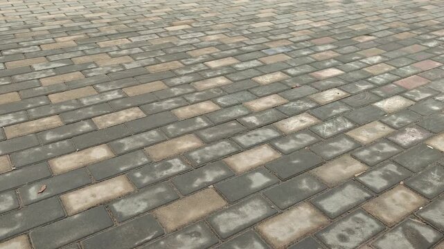 Close-up view of textured paving stones on a walkway, showing variations in color and pattern as a person stands nearby, highlighting the surface details and environment