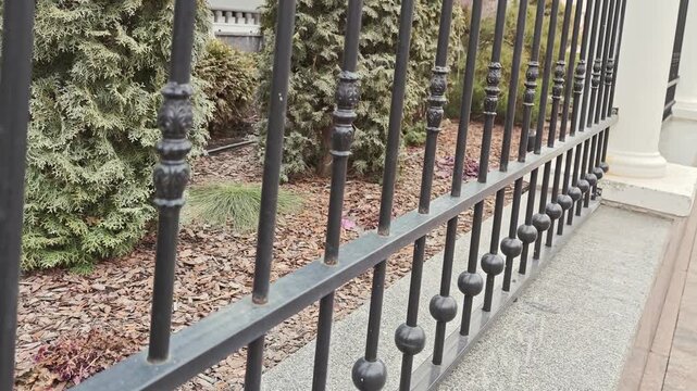 Black wrought iron fence with decorative elements and greenery in the background, showcasing a continuous view of the fence from different angles in an outdoor setting