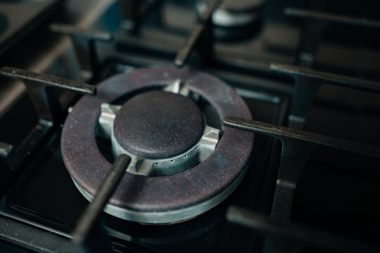 Closeup Of Gas Stove Burner, Worn Metal Grate And Textured Enamel Surface, Dim Neutral Lighting Emphasizes