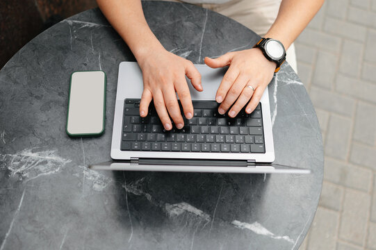 Hands Typing On Laptop At Table, Smartwatch Visible On Wrist, Smartphone Placed Nearby, Marble Surface