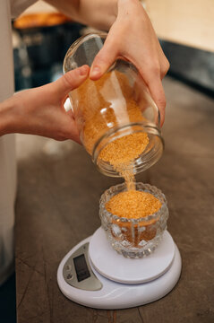 Pouring Yellow Lentils Onto Digital Scale, Hands Steady With Glass Jar And Measuring Cup On Wooden Board, Warm
