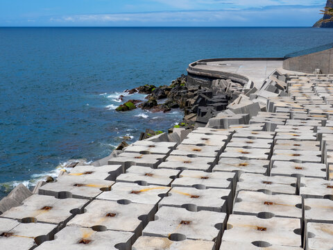 Coastal protection structure made of heavy concrete modules along the shoreline with wave breakers and rugged rocky coast at the ocean (Madeira)