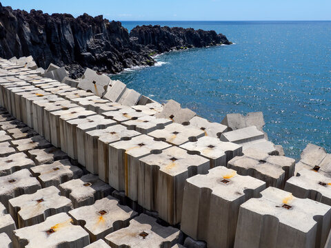Coastal protection structure made of heavy concrete modules along the shoreline with wave breakers and rugged rocky coast at the ocean (Madeira)