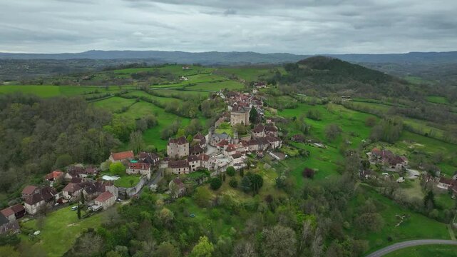 Aerial view of Curemonte France with Saint Hilaire castle and historic village perched on a hill surrounded by lush green rolling countryside under cloudy sky