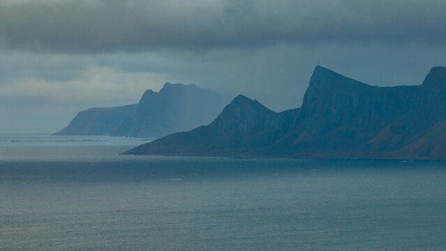 Aerial view of the dramatic mountain peaks and steep cliffs of the Lofoten islands rising from the sea under a moody sky Nordland, Norway.