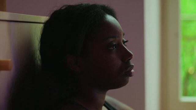 African American woman close up profile by window with distant gaze expressing sadness dissatisfaction and emotional emptiness while feeling lost and aimless indoors
