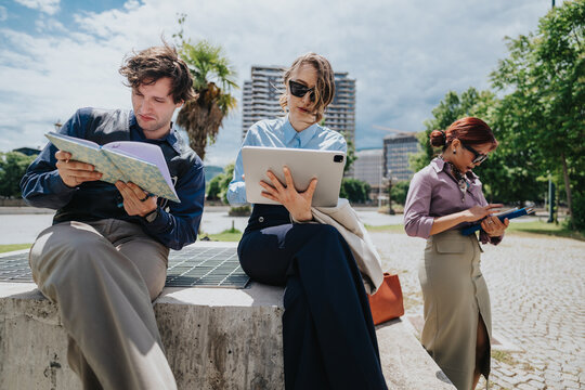 Three business coworkers work with a tablet and notebooks while sitting outdoors. A casual urban meeting scene shows professionals using devices and taking notes in a park.