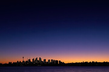 Naklejka premium City skyline silhouetted against a twilight gradient sky over water