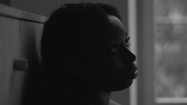 African American woman black and white close up by window with hollow gaze expressing severe depression despair emotional numbness and psychological withdrawal indoors