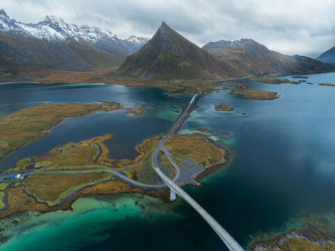 Aerial view of the Fredvang Bridges connecting small islands over turquoise water with dramatic snow-capped mountains in the background Fredvang, Nordland, Norway.