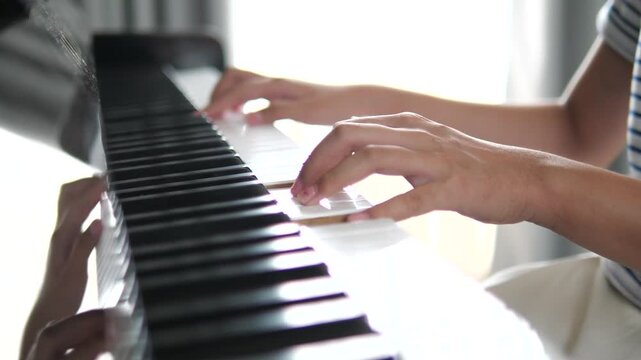 Side view close-up of young girl's hands playing black and white piano keys in a bright room for music education, talent, and aesthetic concept