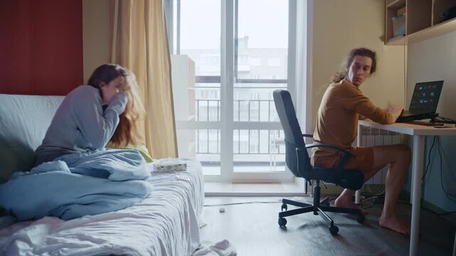 Anxious man stops working to check his sick girlfriend's fever and give her medicine in bed
