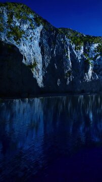 Under the soft glow of moonlight, rugged cliffs stand tall, casting dark silhouettes over calm waters. The serene scene evokes a sense of peace and mystery in the night.
