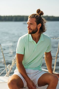 Caucasian male young adult longhair beard on sailboat by the lake relaxed summer portrait with manbun and casual style