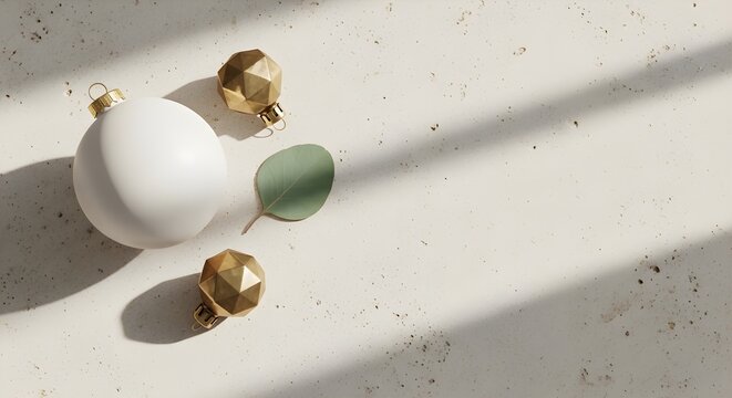 Minimalist holiday arrangement with a white bauble, gold geometric ornaments, and a green leaf on stone.