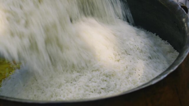 Close-up pouring rice into large kazan for Uzbek plov with sliced carrots