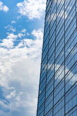 Fototapeta premium Clean and minimalist architectural detail of high-rise building glass panels reflecting clear sky and clouds for business and real estate background