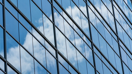 Clean and minimalist architectural detail of high-rise building glass panels reflecting clear sky and clouds for business and real estate background © NewSaetiew