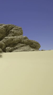 Enormous rock formations tower over the soft, golden sands, creating a stunning contrast. The clear blue sky adds to the serene beauty of this tranquil desert landscape.
